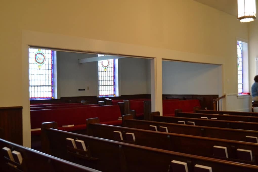 Sanctuary Interior – Left Side View (Before Renovation, 2013) View of Rawls Baptist Church sanctuary before renovation, showing red pews, stained glass windows, and partition walls between seating areas.