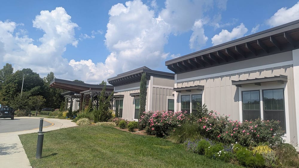 Calys Senior Living Facility Exterior shot with lots of greenery and cloudds on a blue sky filled day.