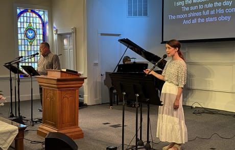 mike_susanna_praise_team Susanna and church member singing on stage with blue light and stained glass in the background