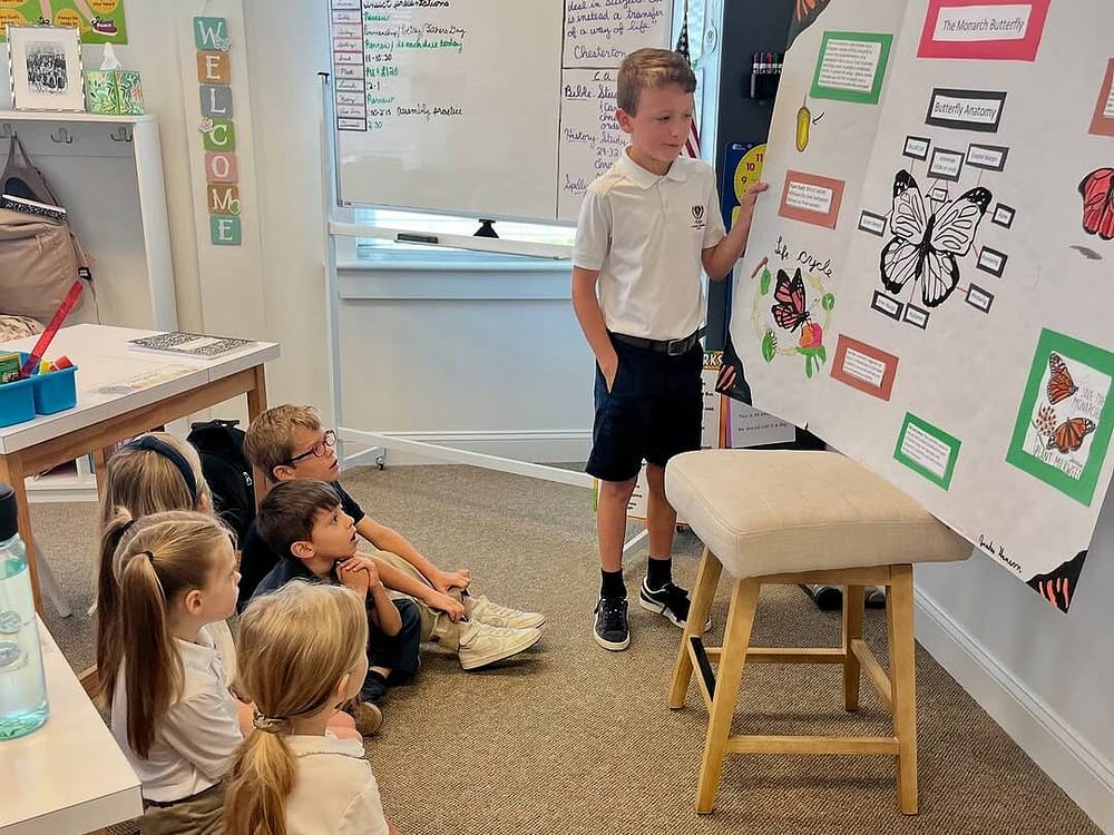 Boy showing assignment to other students at Velos Classical Christian School at Rawls Baptist Church
