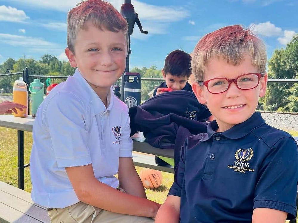Velos Classical Christian School Kids Sitting Outside in Sunny Weather Smiling