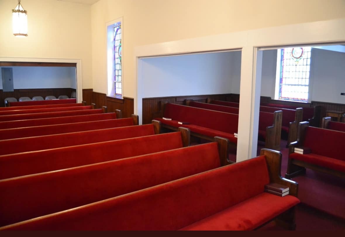 Sanctuary Seating – Angled View (Before Renovation, 2013) Rawls Baptist Church sanctuary prior to renovation, showing the arrangement of red pews and wooden trim beneath stained glass windows.