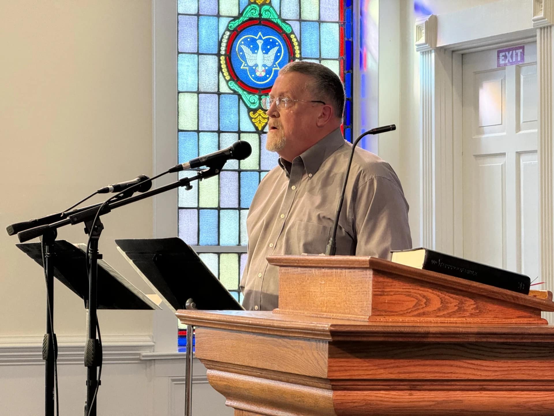 Church member singing into microphone with a stained glass window behind him illuminated,