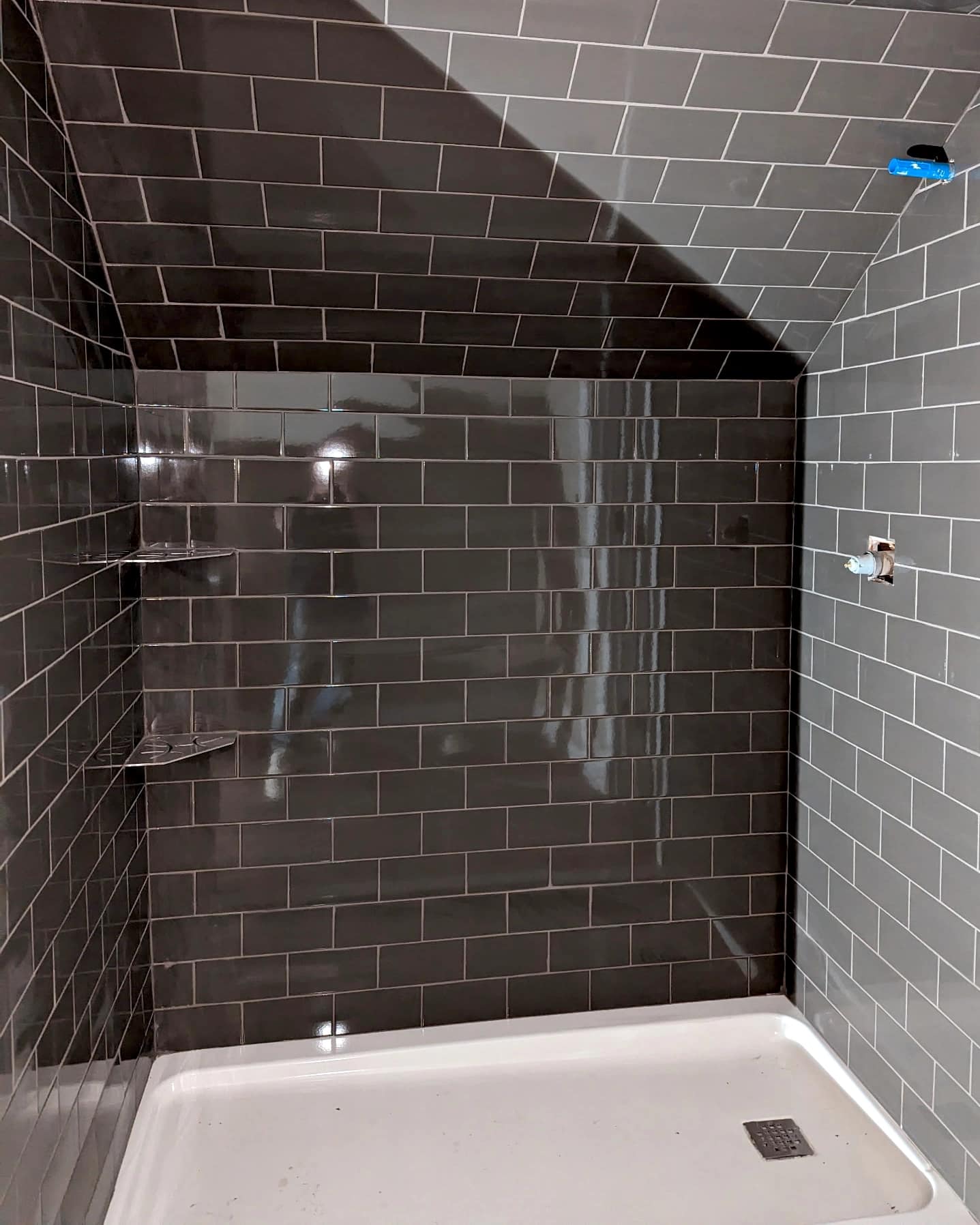 Glossy gray subway tile shower with an angled ceiling and corner shelving.