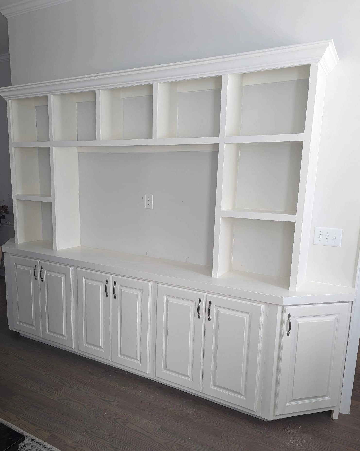 Custom white built-in entertainment center with open shelving, crown molding, and lower cabinet storage.