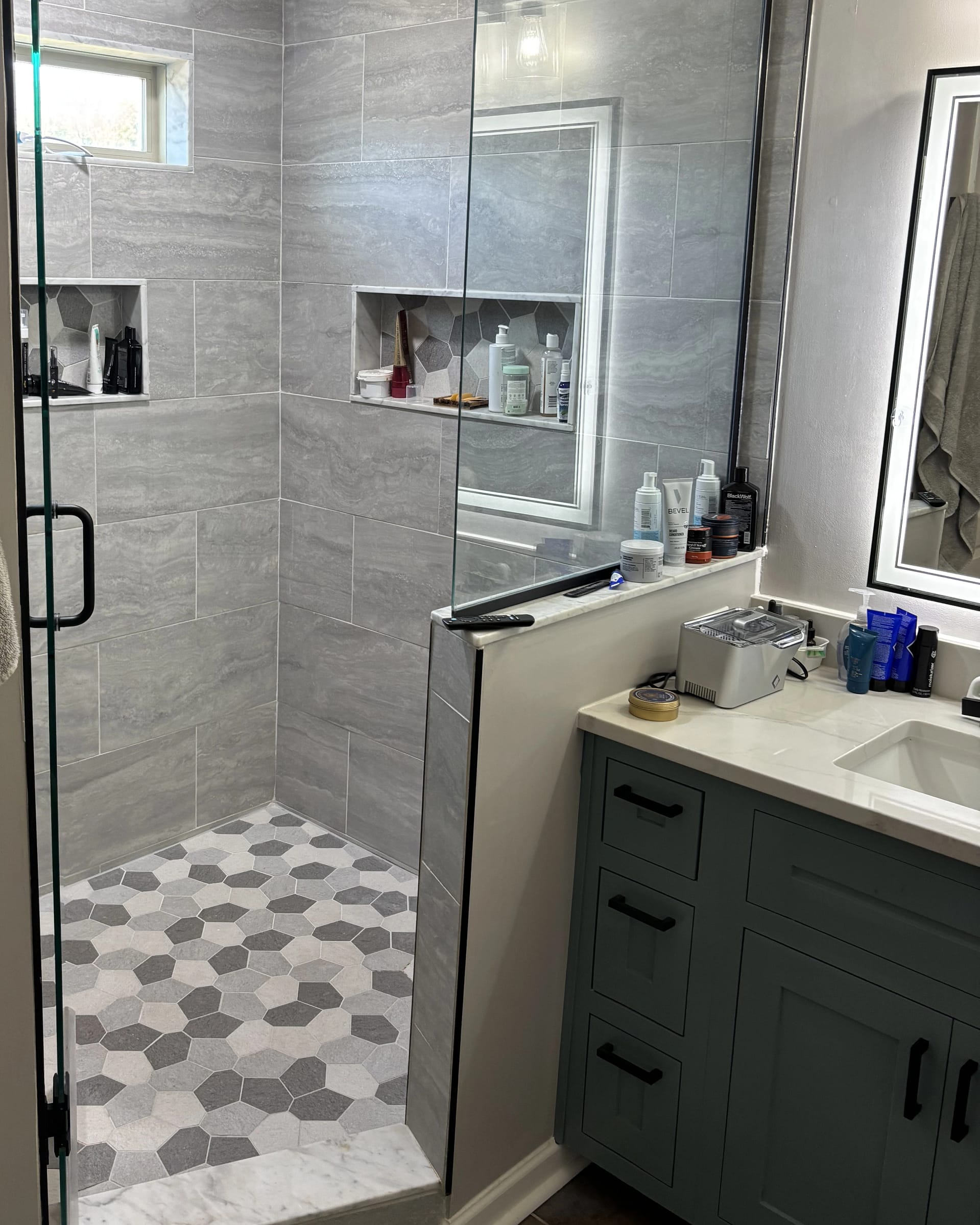 Walk-in shower with gray wall tile and contrasting hexagon tile floor pattern.