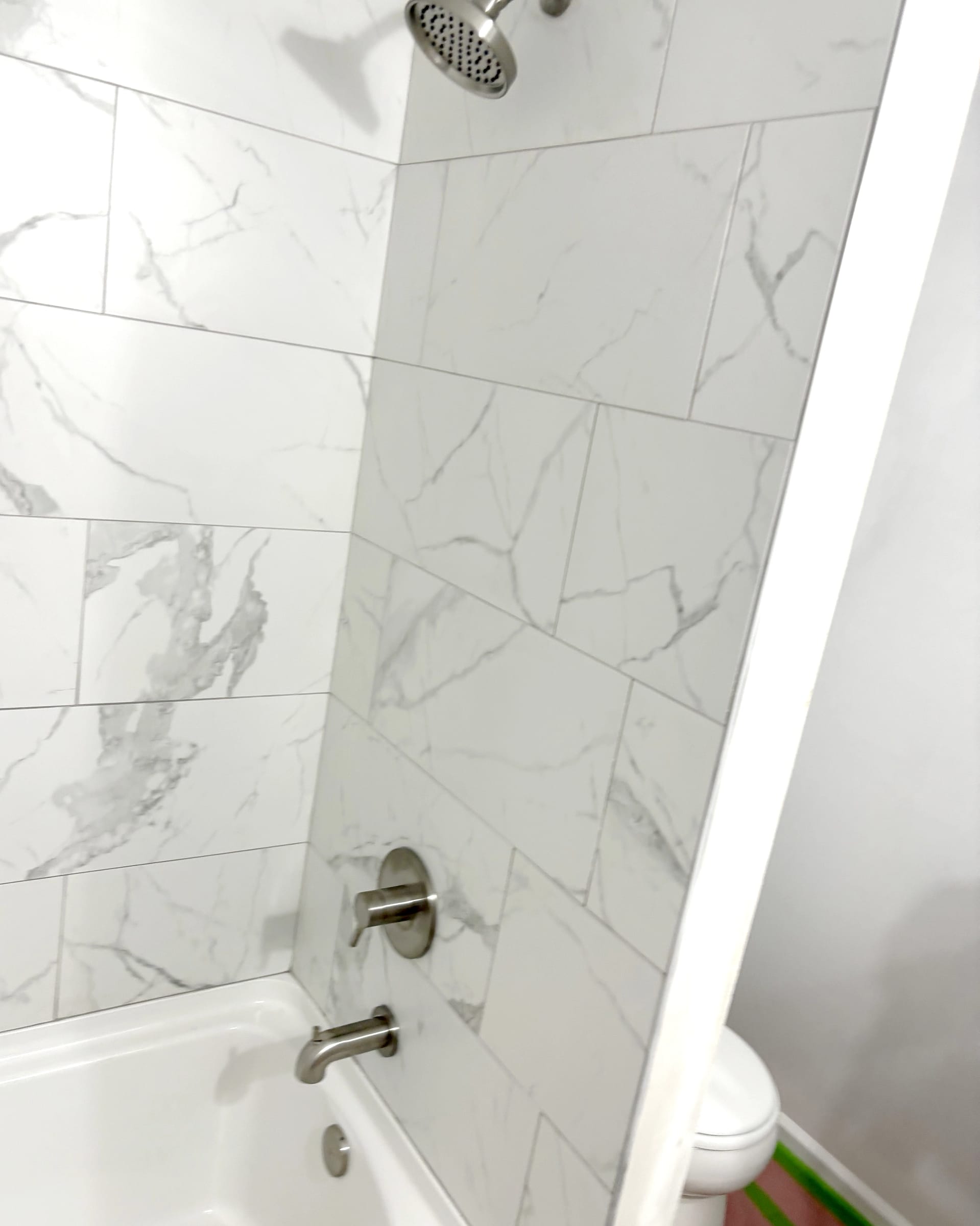 White tub-and-shower surround with large marble-look tile and brushed nickel fixtures.