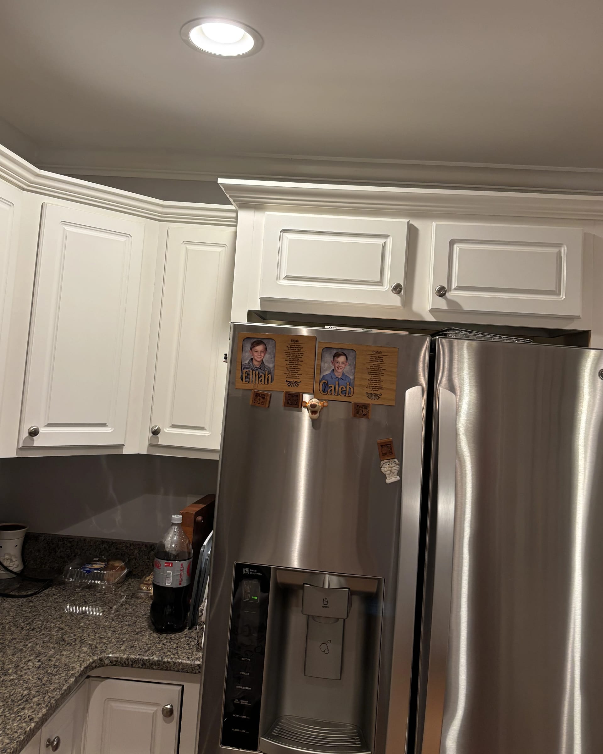 White shaker kitchen cabinetry surrounding stainless refrigerator with crown molding above.