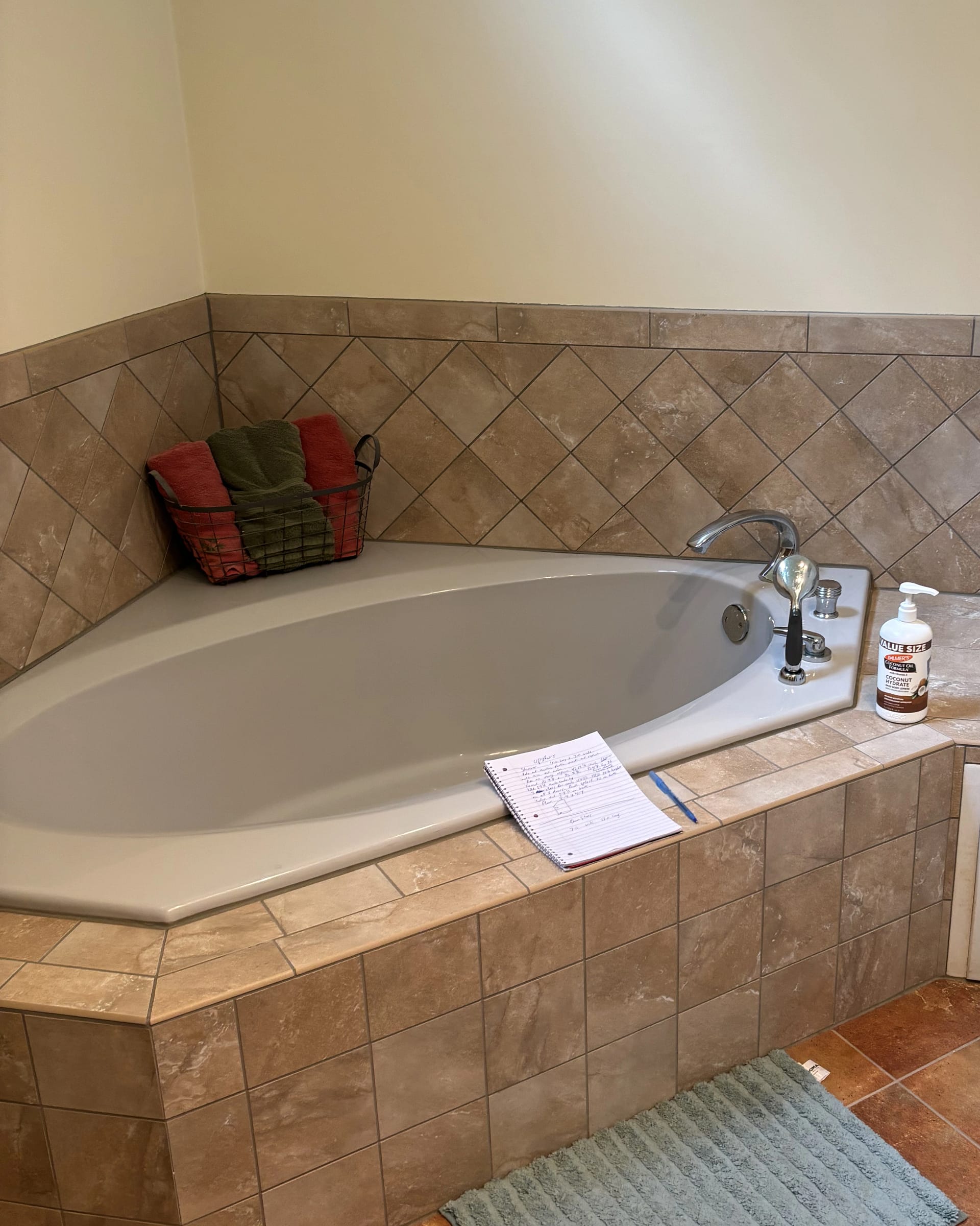 Corner jetted bathtub with tan ceramic tile surround and diagonal wall tile pattern.