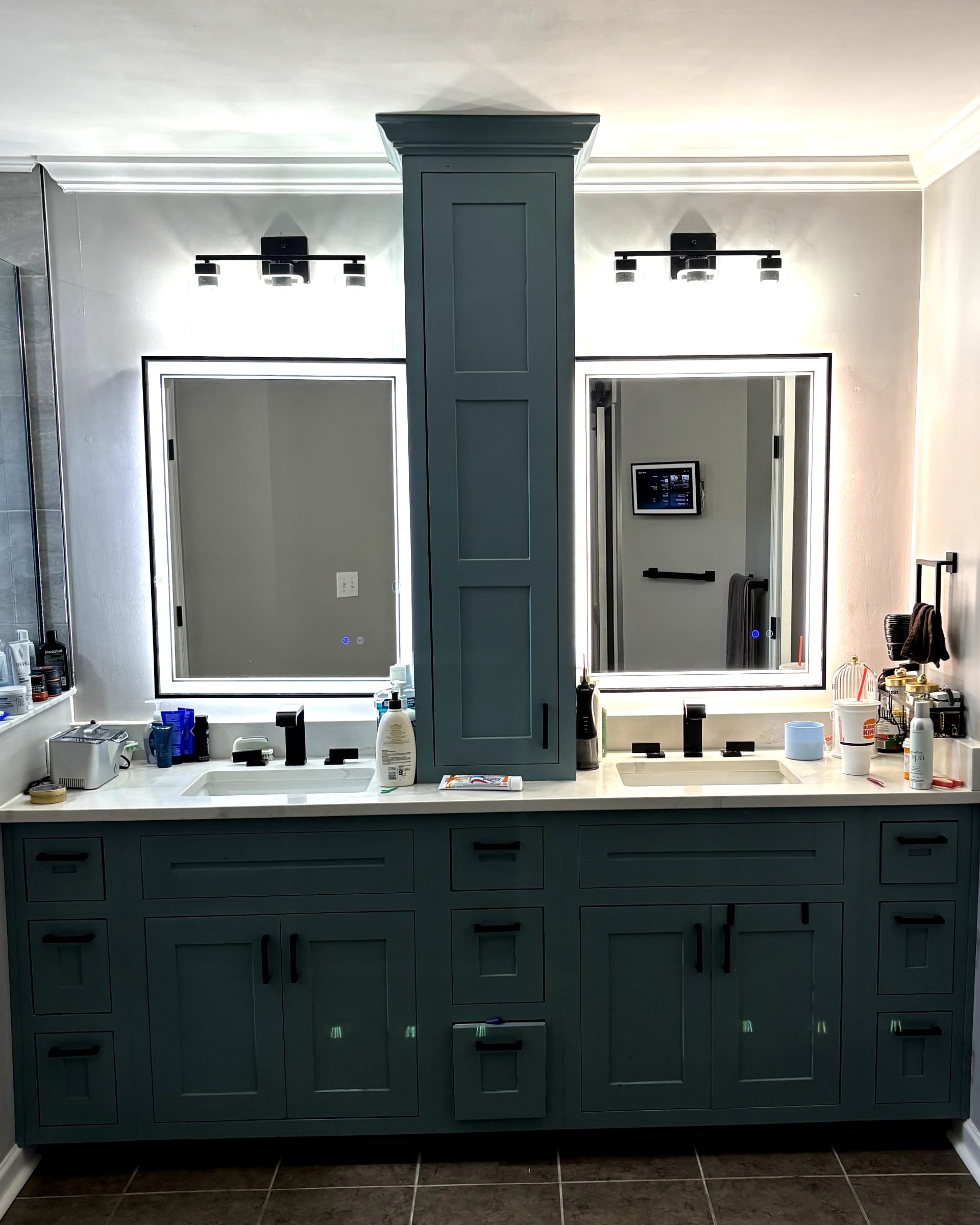 Teal double-sink vanity with center tower cabinet, black hardware, and LED backlit mirrors.