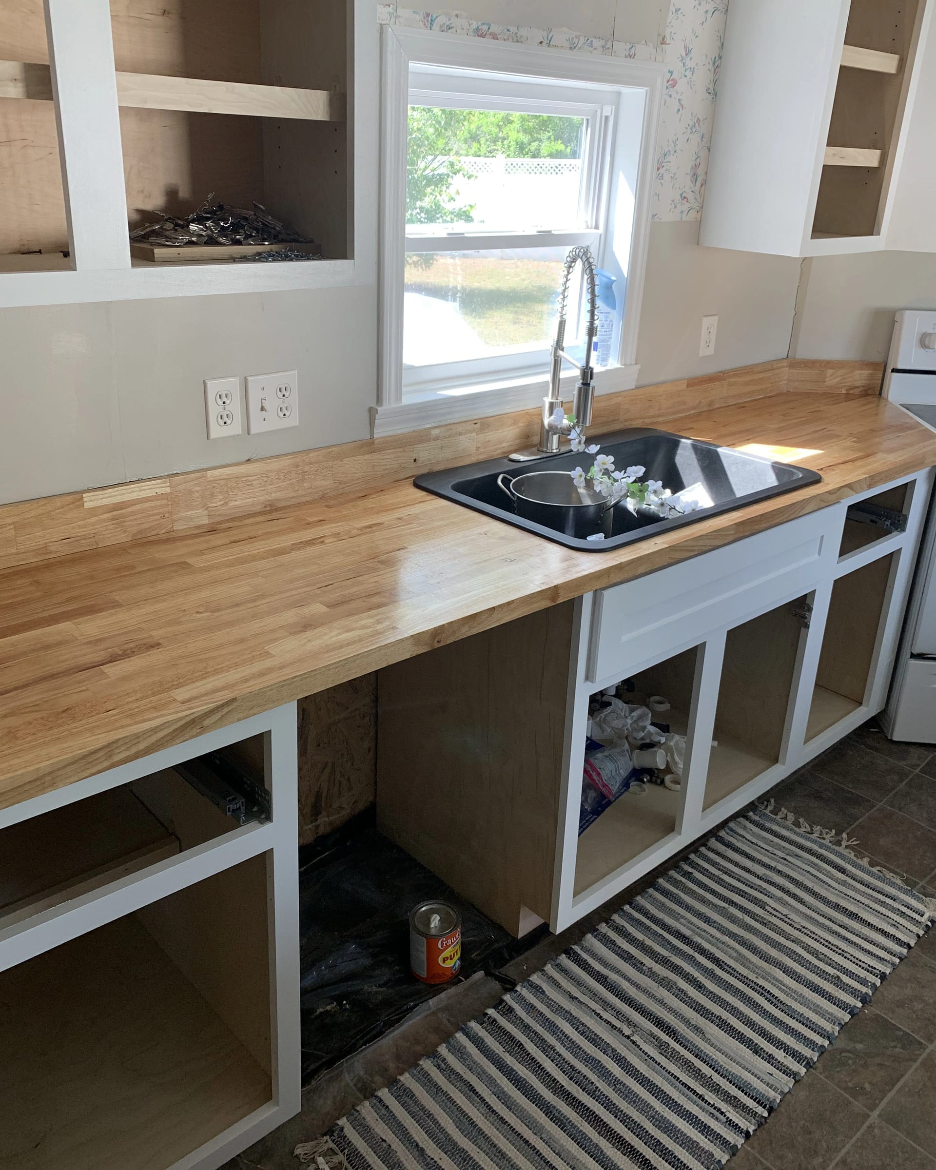 Kitchen renovation with butcher-block counters, new sink installation, and partially finished backsplash.