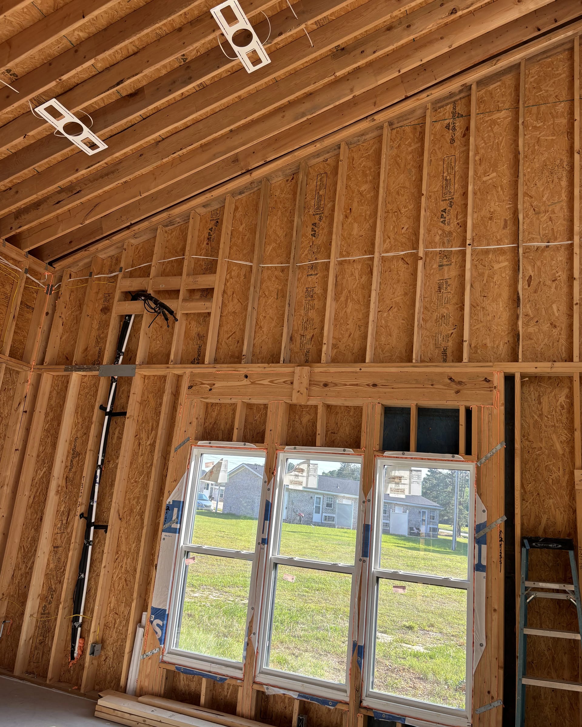 New construction wall with triple windows framed in and open ceiling joists above.