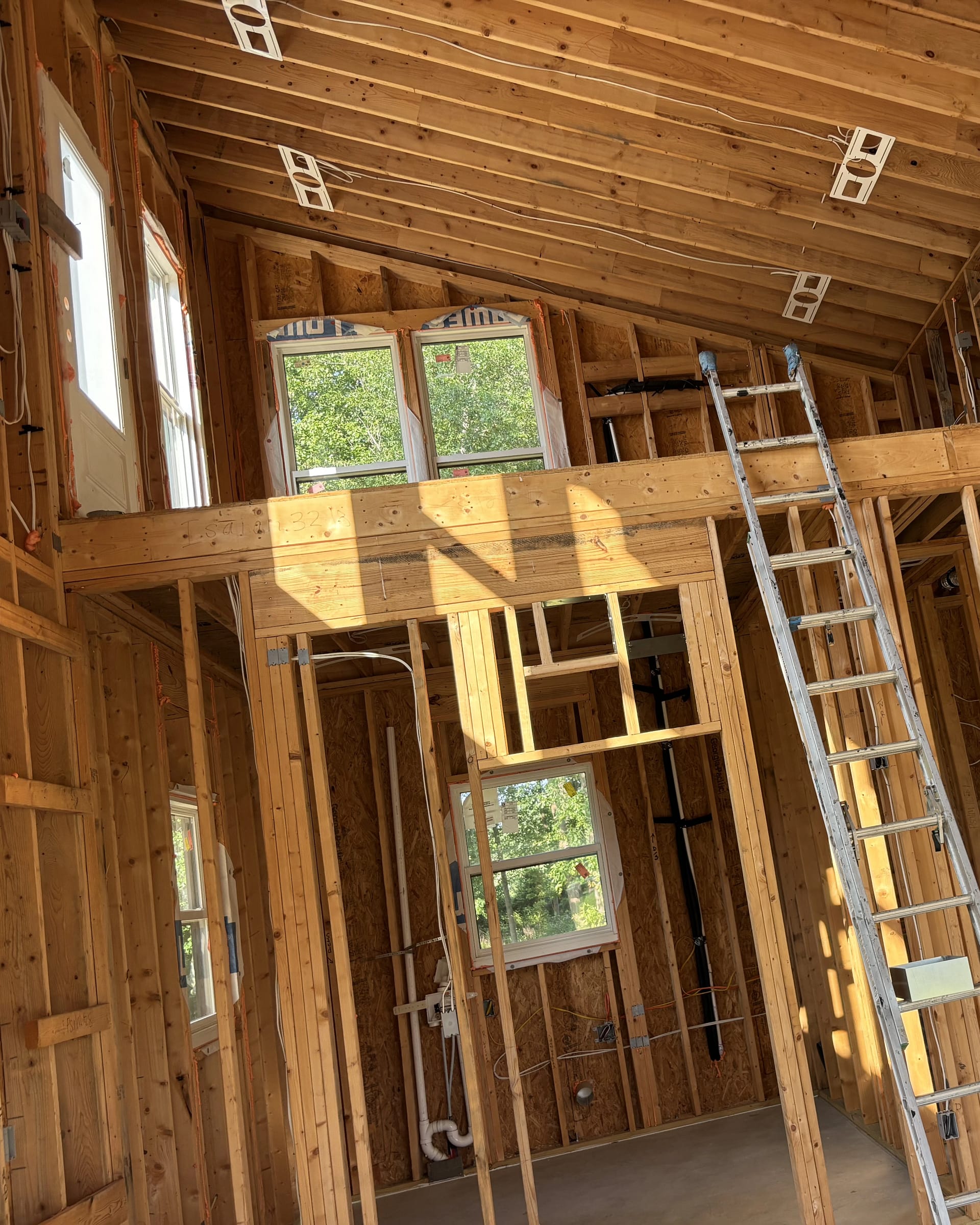 Loft framing with multiple windows, exposed joists, and ladder access during renovation.