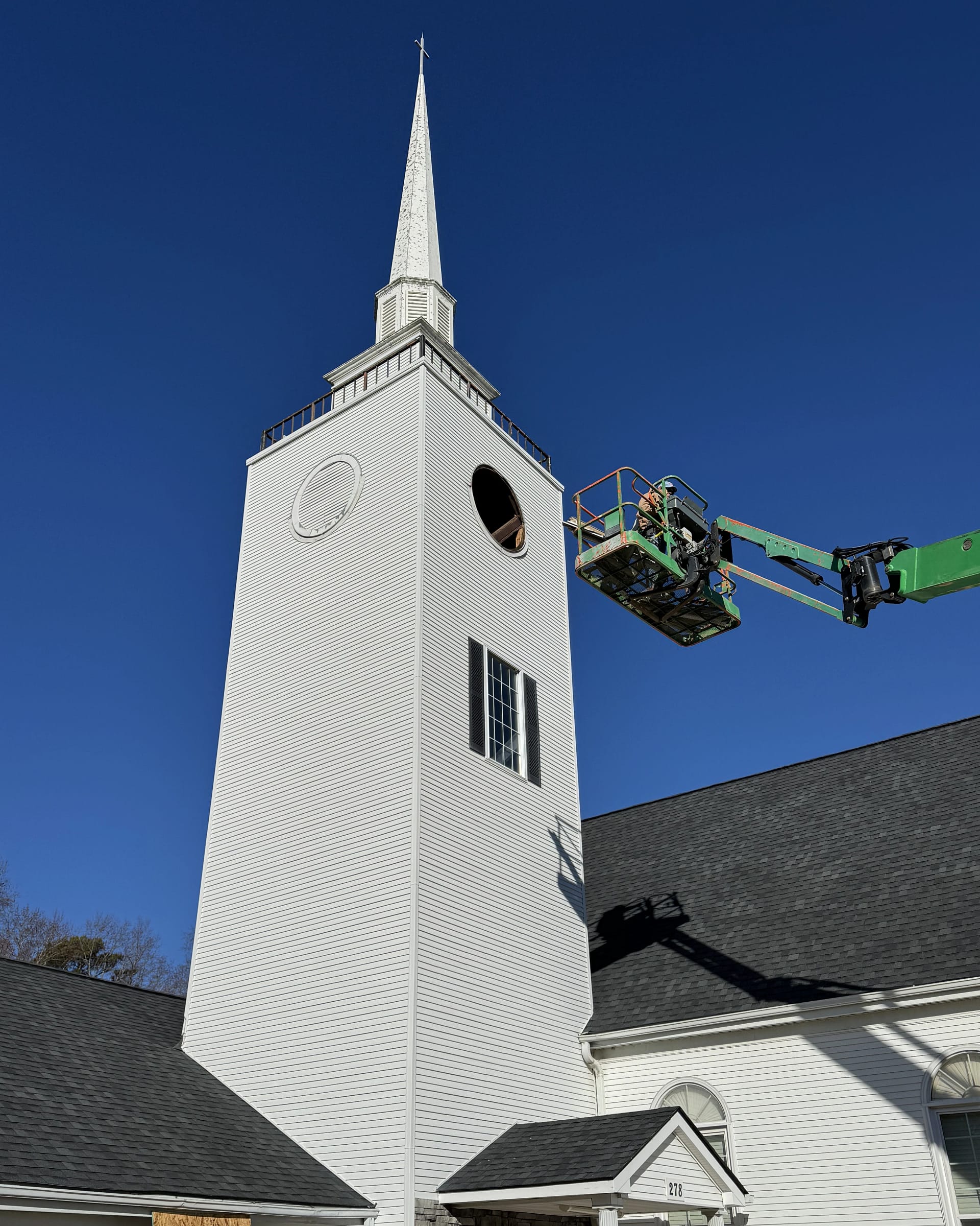 Church steeple fascia repair underway with workers accessing the upper section via lift equipment.