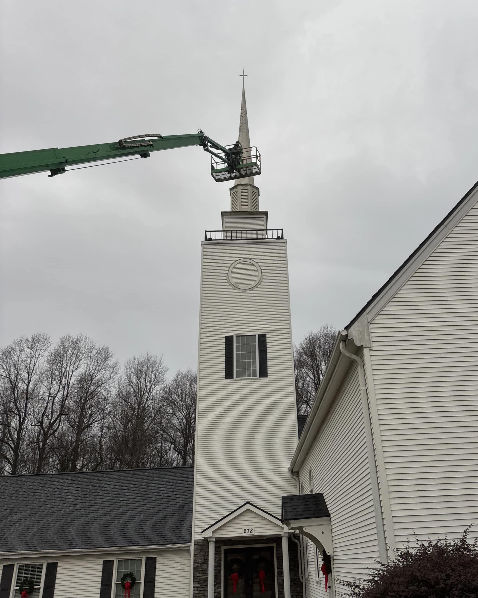 Church steeple restoration in progress using a hydraulic lift to access upper trim and siding.