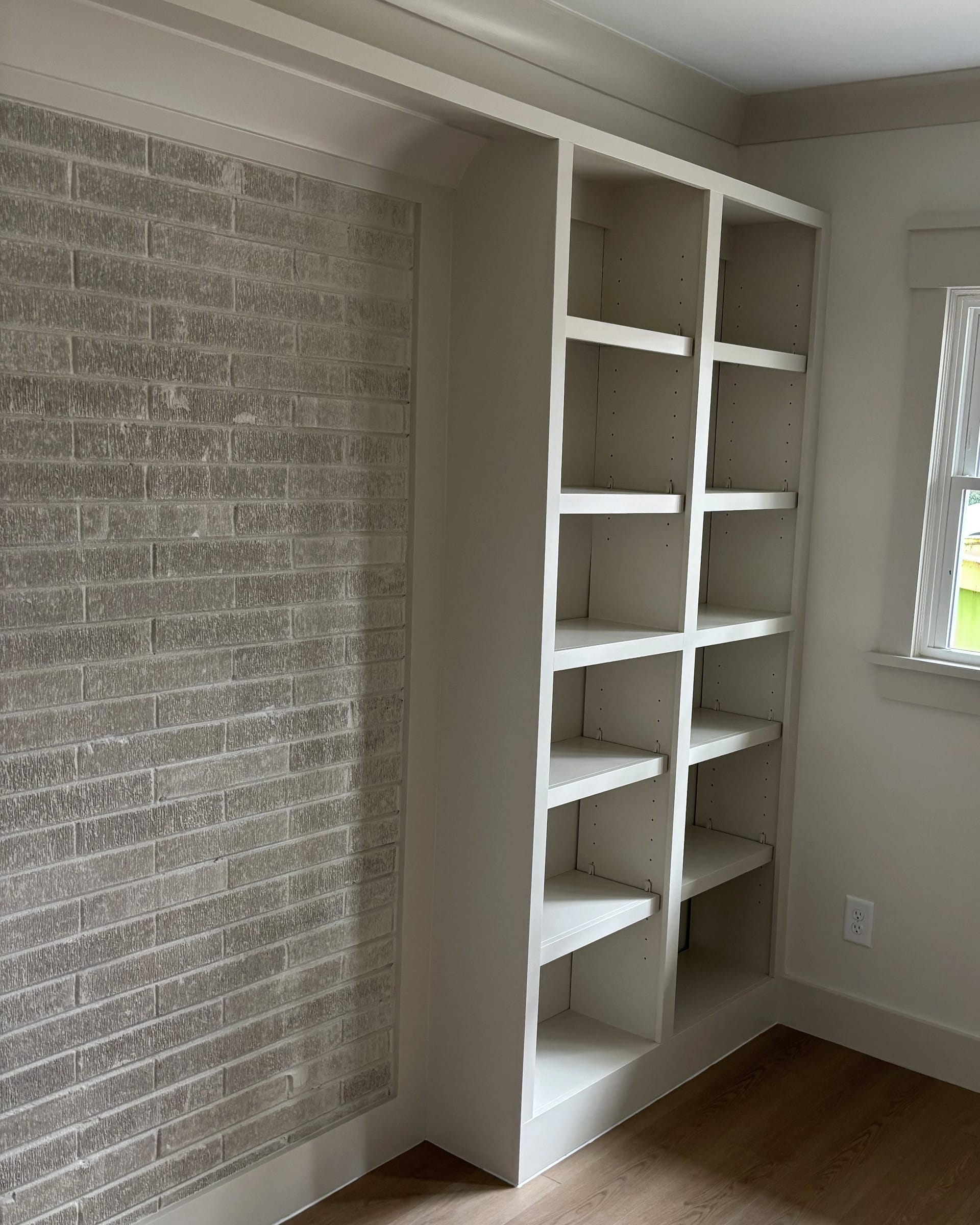 White built-in shelving unit beside brick accent wall with adjustable shelves.