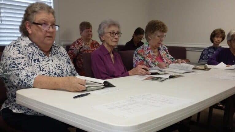 Women's Sunday School class with women sitting at a table paying attention intently.
