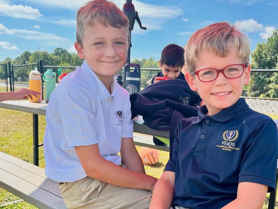 Velos Classical Christian School Kids Sitting Outside in Sunny Weather Smiling